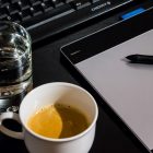 Office desk setup with a coffee cup, glass of water, tablet, pen, and keyboard.