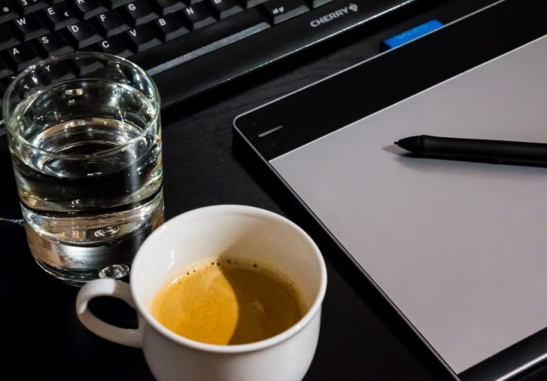 Office desk setup with a coffee cup, glass of water, tablet, pen, and keyboard.