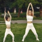 Mother and daughter in matching activewear doing exercises outdoors on a sunny day.